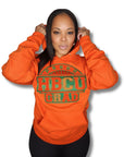 “Woman wearing an orange hoodie with green PROUD HBCU GRAD lettering against a white background.”
