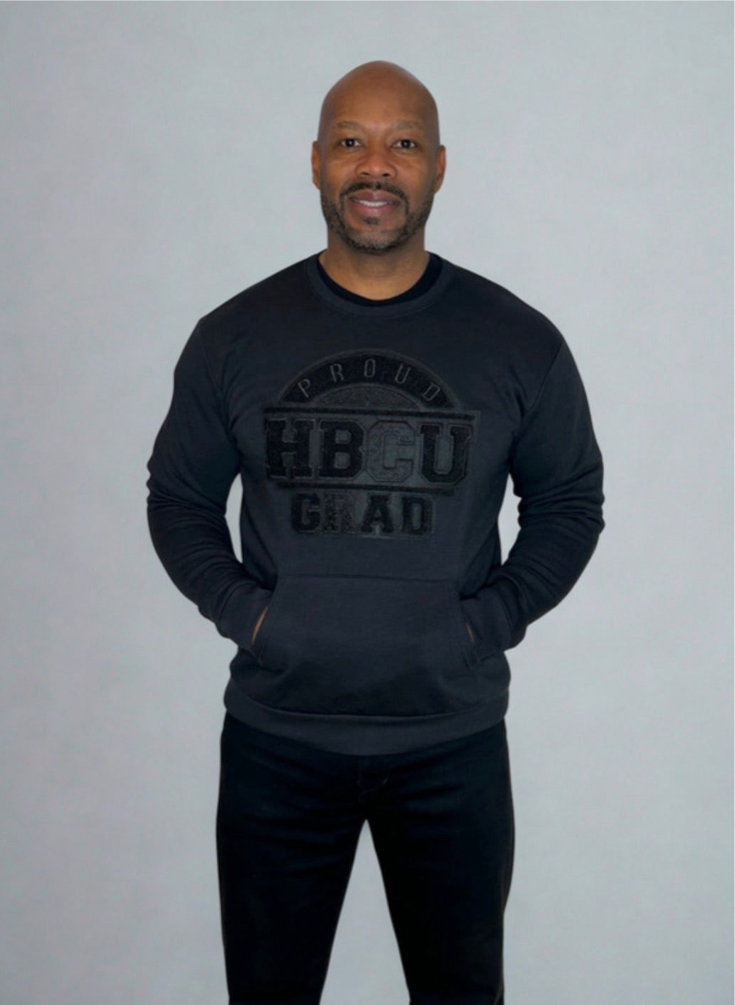 Man wearing an all-black Proud HBCU Grad sweatshirt featuring a hand-stitched chenille patch and front pockets, designed to celebrate HBCU pride and legacy