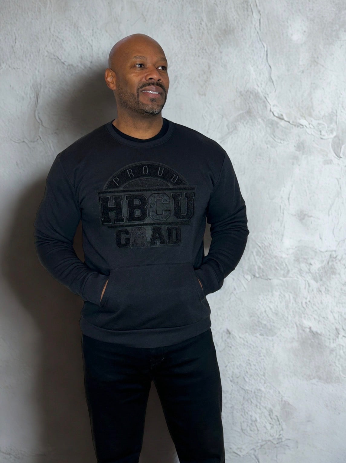 Man wearing an all-black Proud HBCU Grad sweatshirt featuring a hand-stitched chenille patch and front pockets, designed to celebrate HBCU pride and legacy