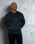 Man wearing an all-black Proud HBCU Grad sweatshirt featuring a hand-stitched chenille patch and front pockets, designed to celebrate HBCU pride and legacy