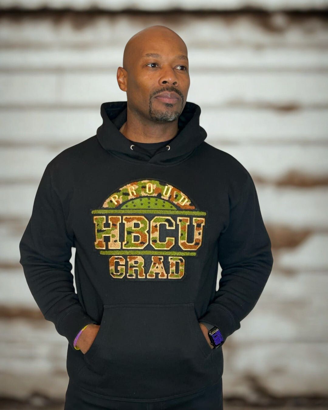 Model wearing a black Proud HBCU Grad hoodie with a handcrafted camo chenille patch, varsity-style stitched lettering.